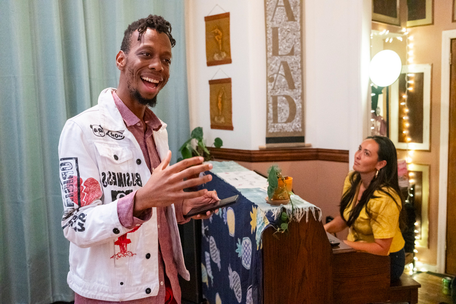 Brenton Zola performs during the fourth installment of Salad, gesturing and speaking in the foreground, while behind him to the right, Salad's co-founder Sio Tepper accompanies the performance on piano.